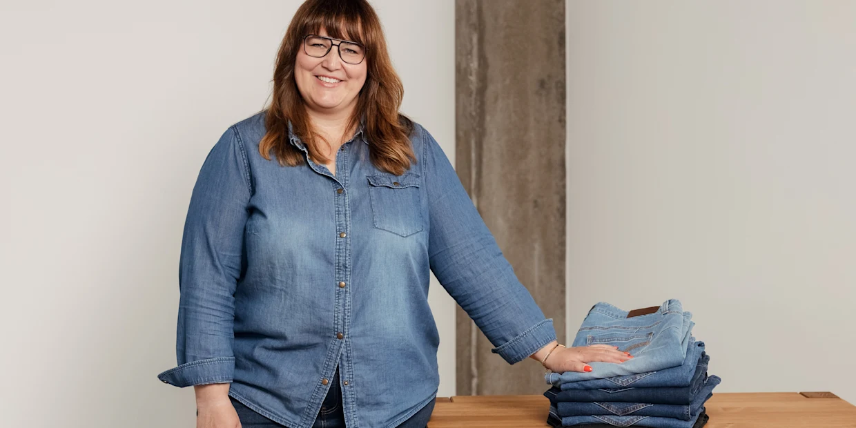 Frau steht am Tisch und legt ihre Hand auf einen Stapel Jeans Frau steht am Tisch und legt ihre Hand auf einen Stapel Jeans