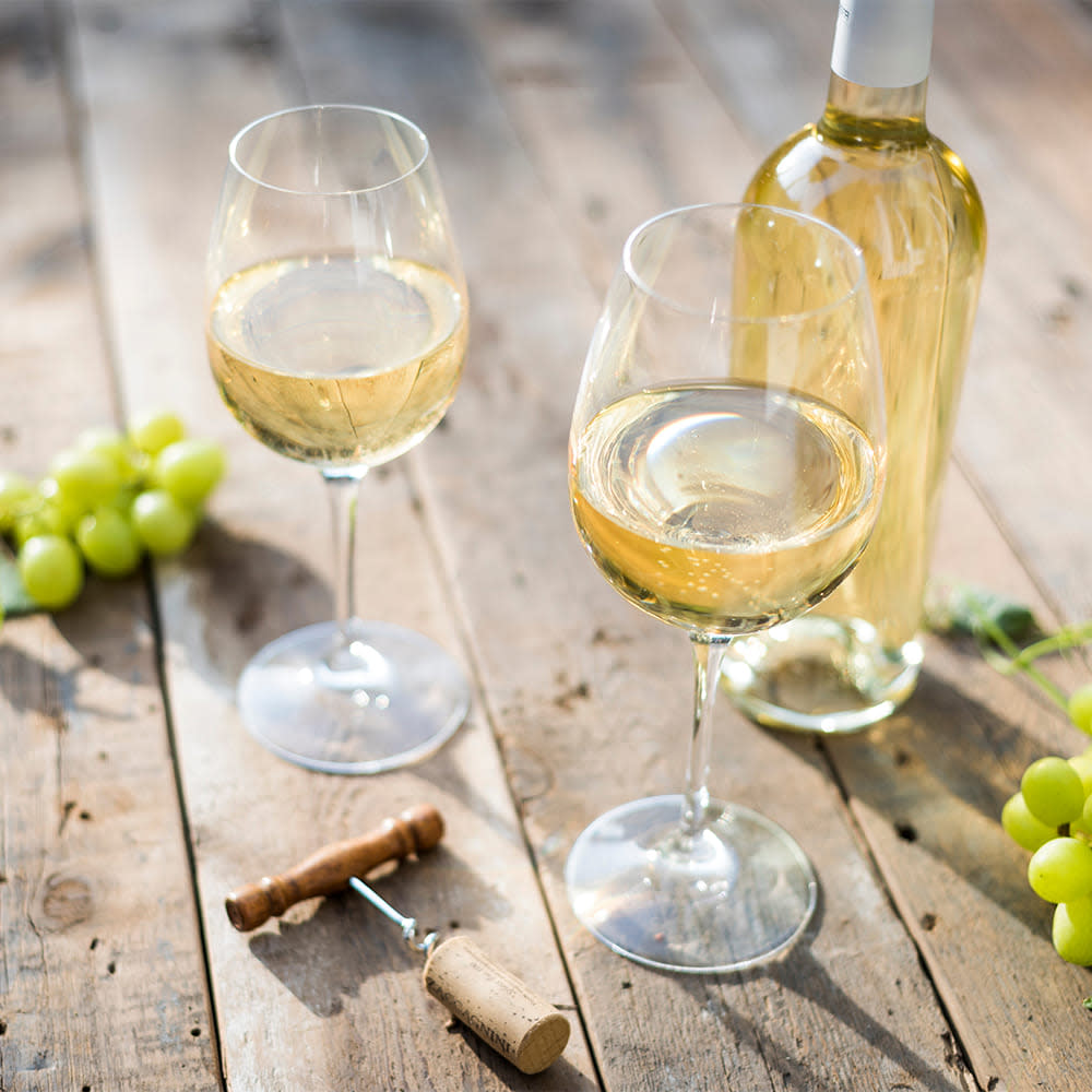 Glasses of white wine next to the bottle on a table surrounded by grapes