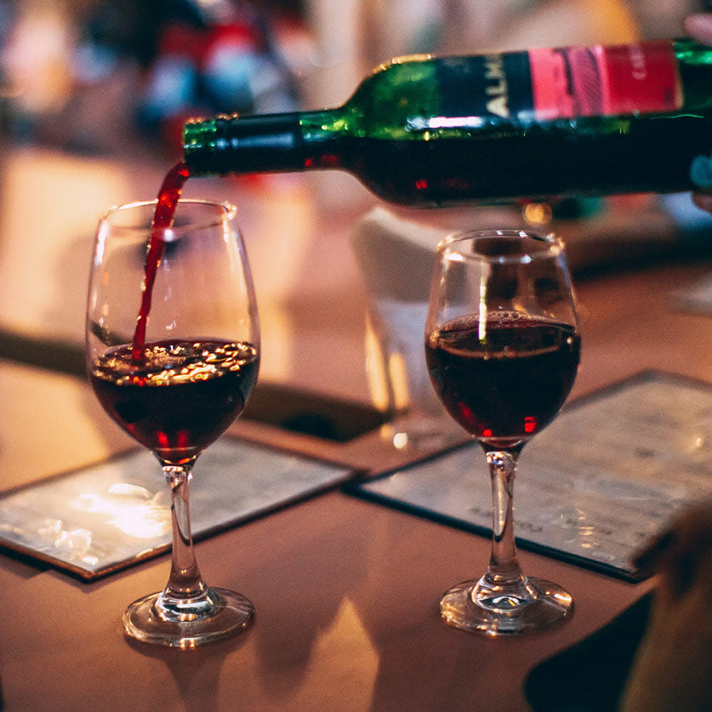 Pouring a glass of red wine at a dinner table, next to one already poured