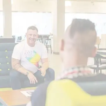 Due persone che parlano. Una indossa una maglia rainbow.