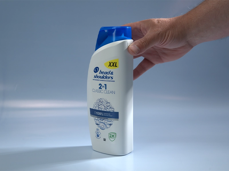 Un flacone di Head & Shoulders in cui sono visibili i simboli tattili, 4 sottili linee in rilievo sul fianco del flacone, accarezzati dal pollice della mano destra di un signore