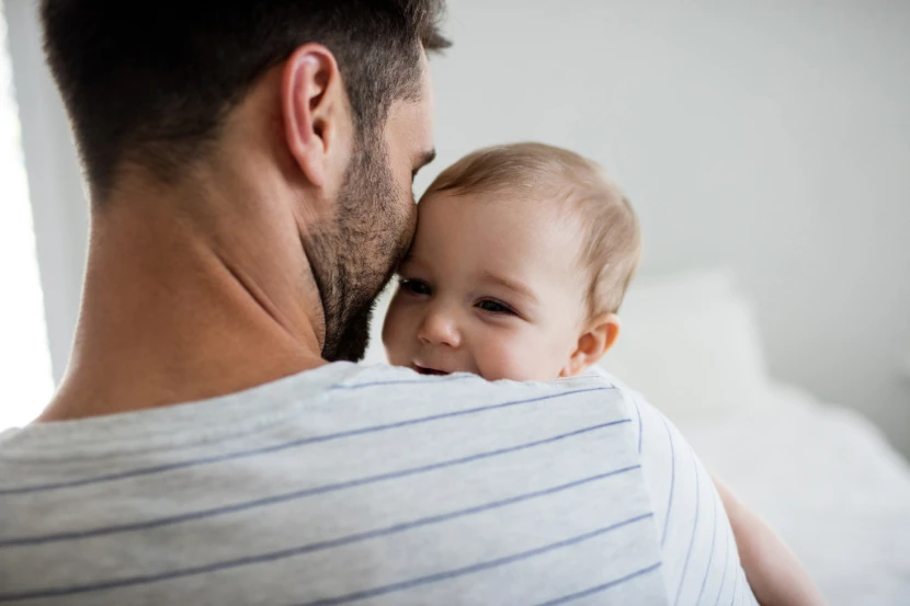 Un papà di spalle tiene in braccio un neonato che sorride