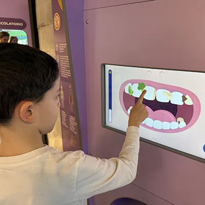Un bambino di 7 anni gioca con un touch screen: con il dito simula lo spazzolamento e rimuovere lo sporco dai denti.