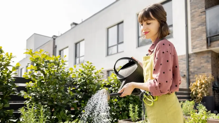 Una donna innaffia il giardino di casa, prestando attenzione al consumo di risorse per rendere la propria casa più sostenibile