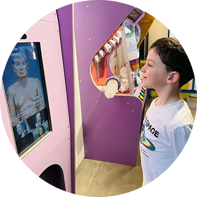 Un bambino di 7 anni guarda verso uno schermo con videocamera e sorride mostrando orgogliodamente i suoi denti.