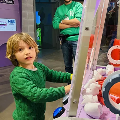 Un bambino guarda in camera e sorride mentre preme i bottoni alla base dell’installazione che illuminano le aree della lingua che identificano i sapori. 