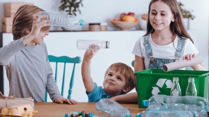 Tre bambini inseriscono delle bottiglie di plastica all’interno di un contenitore per il riciclo.