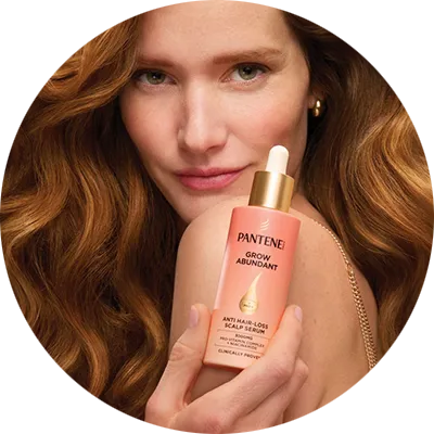 una donna con capelli castani tiene in mano un flacone di pantene grow abundant. I suoi capelli sono folti e lucenti.