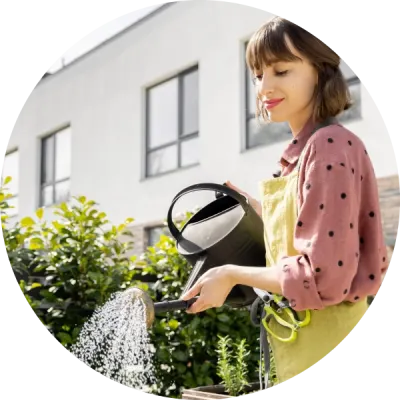 Una donna innaffia il giardino di casa, prestando attenzione al consumo di risorse per rendere la propria casa più sostenibile