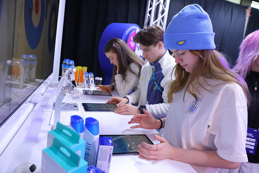 Un gruppo di alteti gioca con i tablet ai giochi di sci alpino e bob nel villaggio virtuale “gioca e vinci” di P&G.