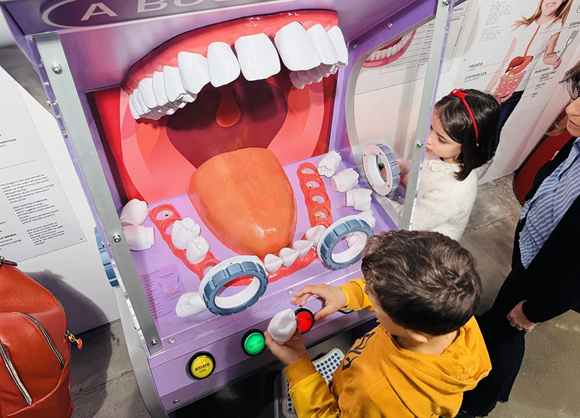 Un bambino di 6 anni indossa una felpa arancione, è fotografo dall’alto mentre gioca con l’installazione: una bocca aperta gigante.