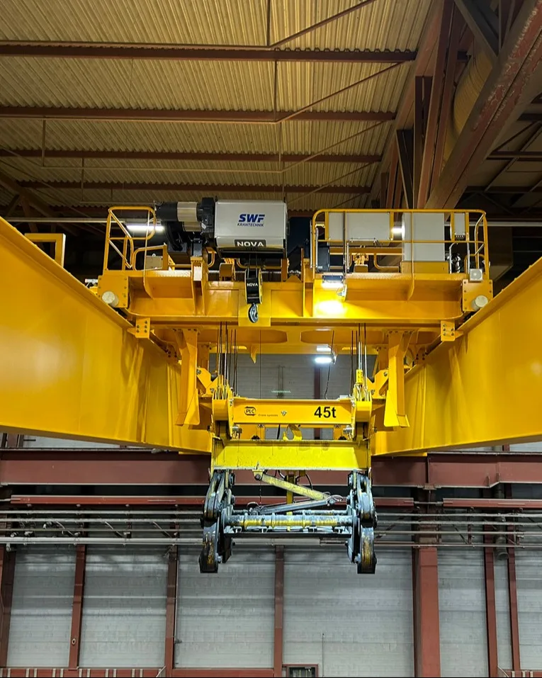 Industrial overhead crane and hoist trolley on rails inside a production hall, used for handling heavy loads.
