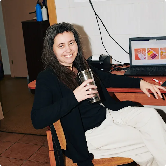 Woman sitting with coffee in front of laptop in small office space.