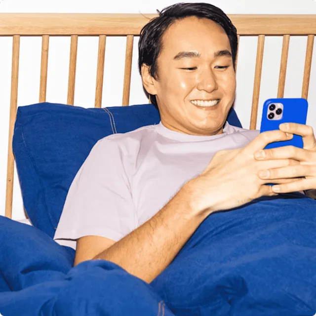 Man laying in his bed with colorful blue bedsheets, looking at this bright blue phone.