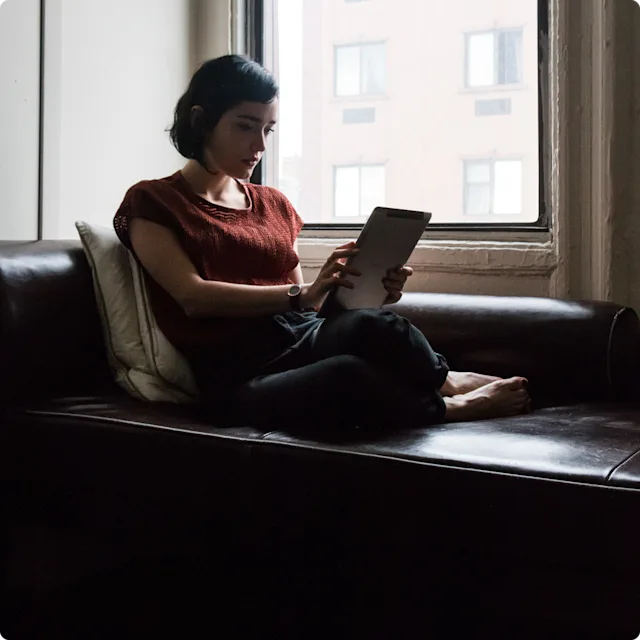 Woman sitting on couch looking at her ipad with futuristic vibe.