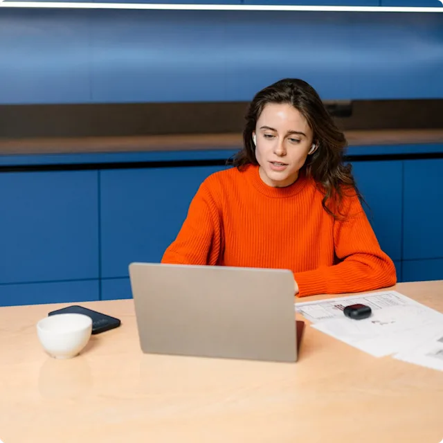Woman in orange sweater sitting in front of labtop