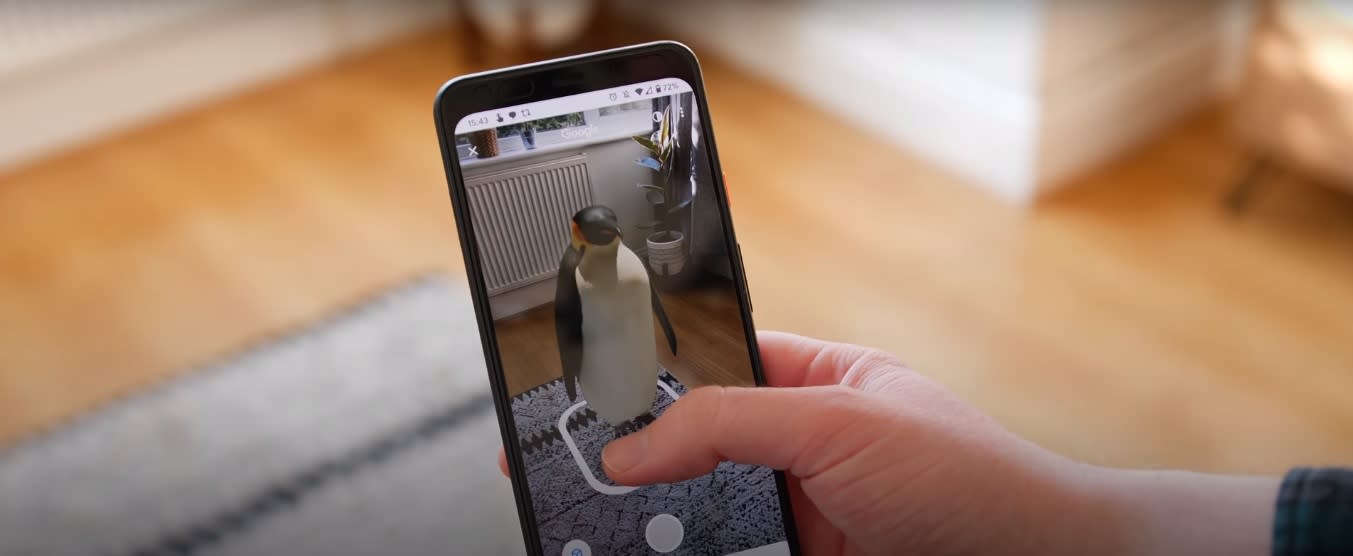 Telefon trzymany w dłoni pokazujący pingwina na tle mieszkania w aplikacji AR