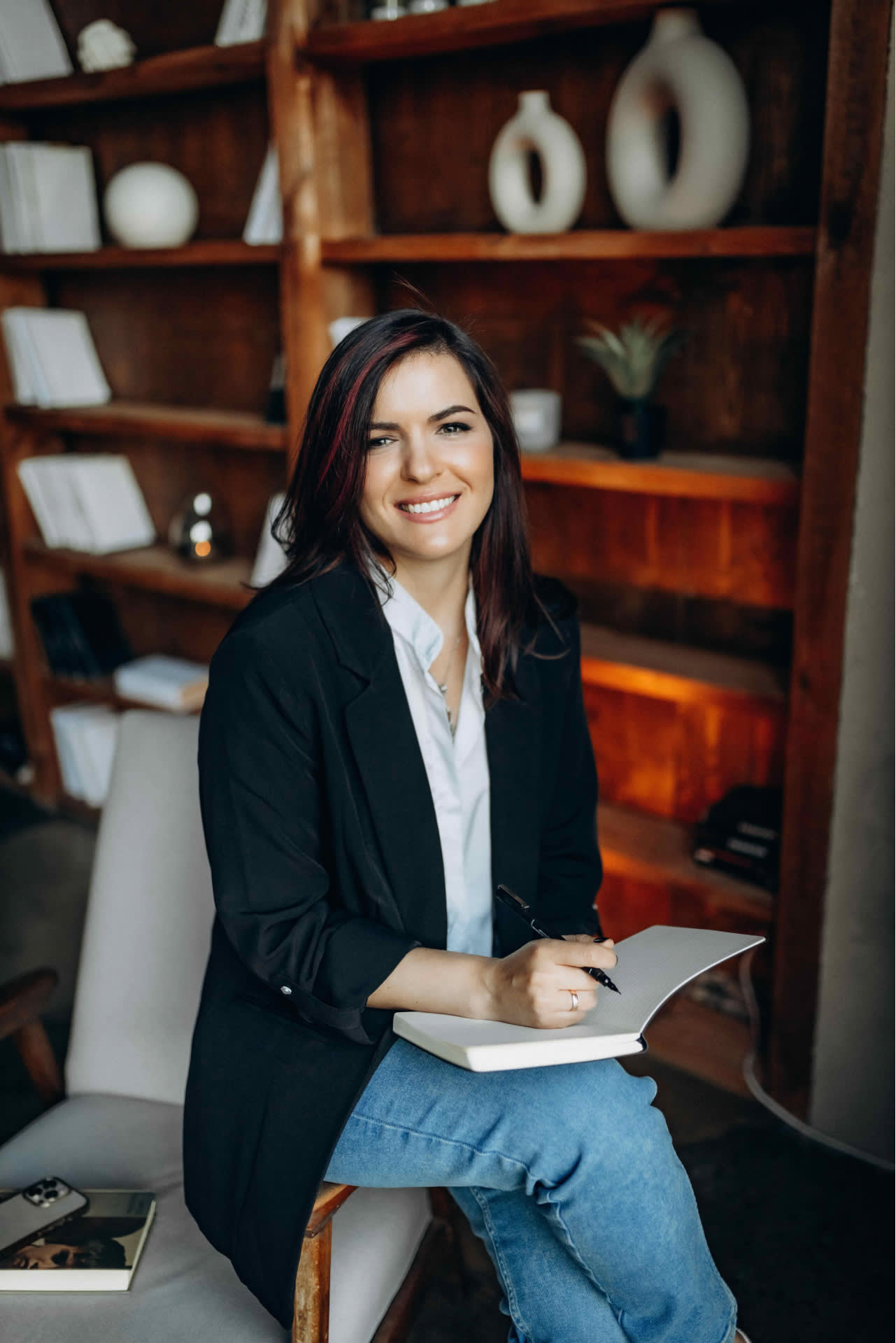 Smiling author is sitting in the chair and holding the notebook.