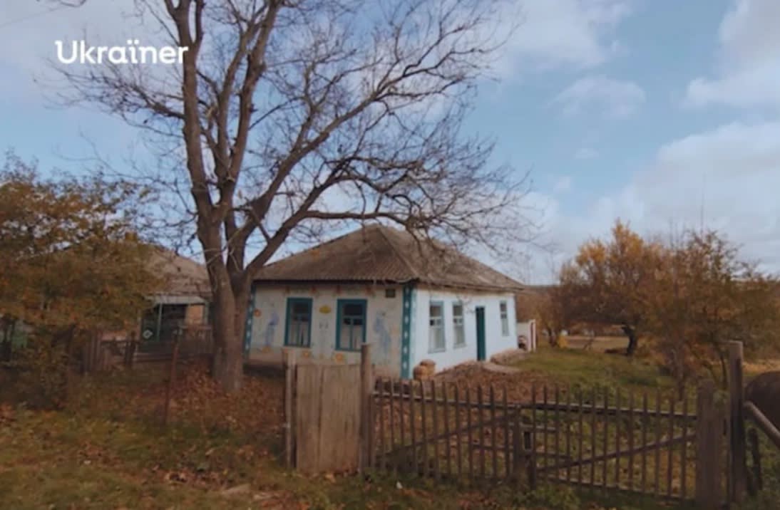 Typical Ukrainian village house of the beginning of the XX century. There is a tall tree near the house. The yard is fenced with an old fence. The picture is taken in autumn time.