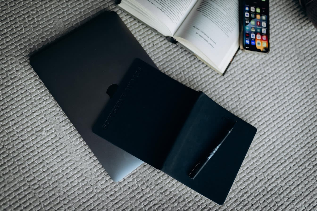 The image reflects the author's working atmosphere. Some tools are chaotically left on the floor, such as opened book, a laptop, a black notebook with a pen, and a mobile phone.