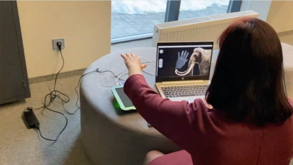 The image shows the woman holding her hand above mid-air haptic device while she is watching at the screen displaying mammut. 