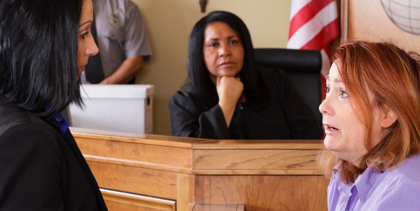white female attorney questioning white female witness in courtroom while black female judge looks on