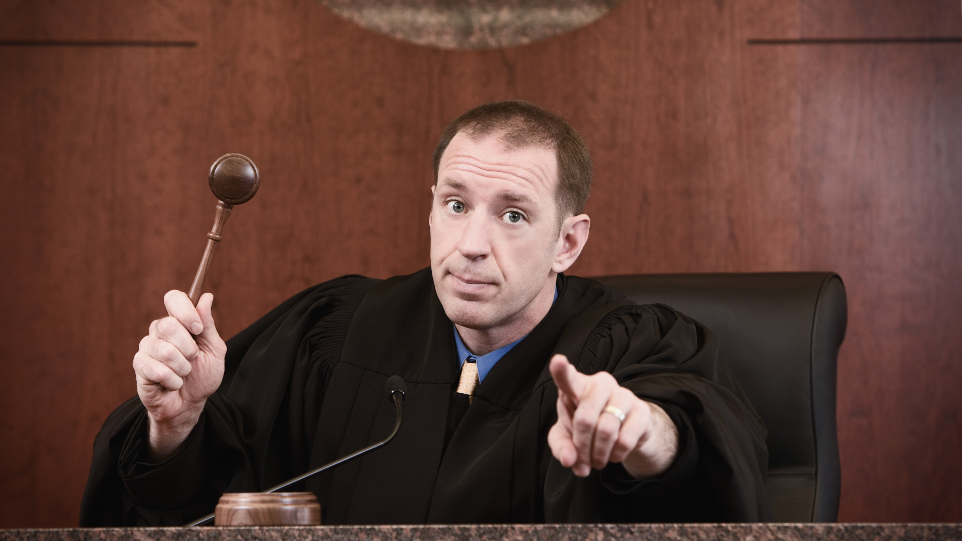 An upset judge holding a gavel and pointing at the court.