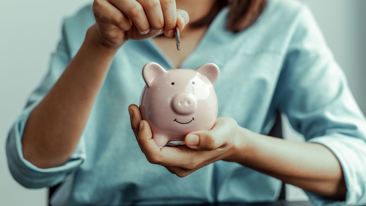 Image of a woman dropping a coin into a piggy bank.