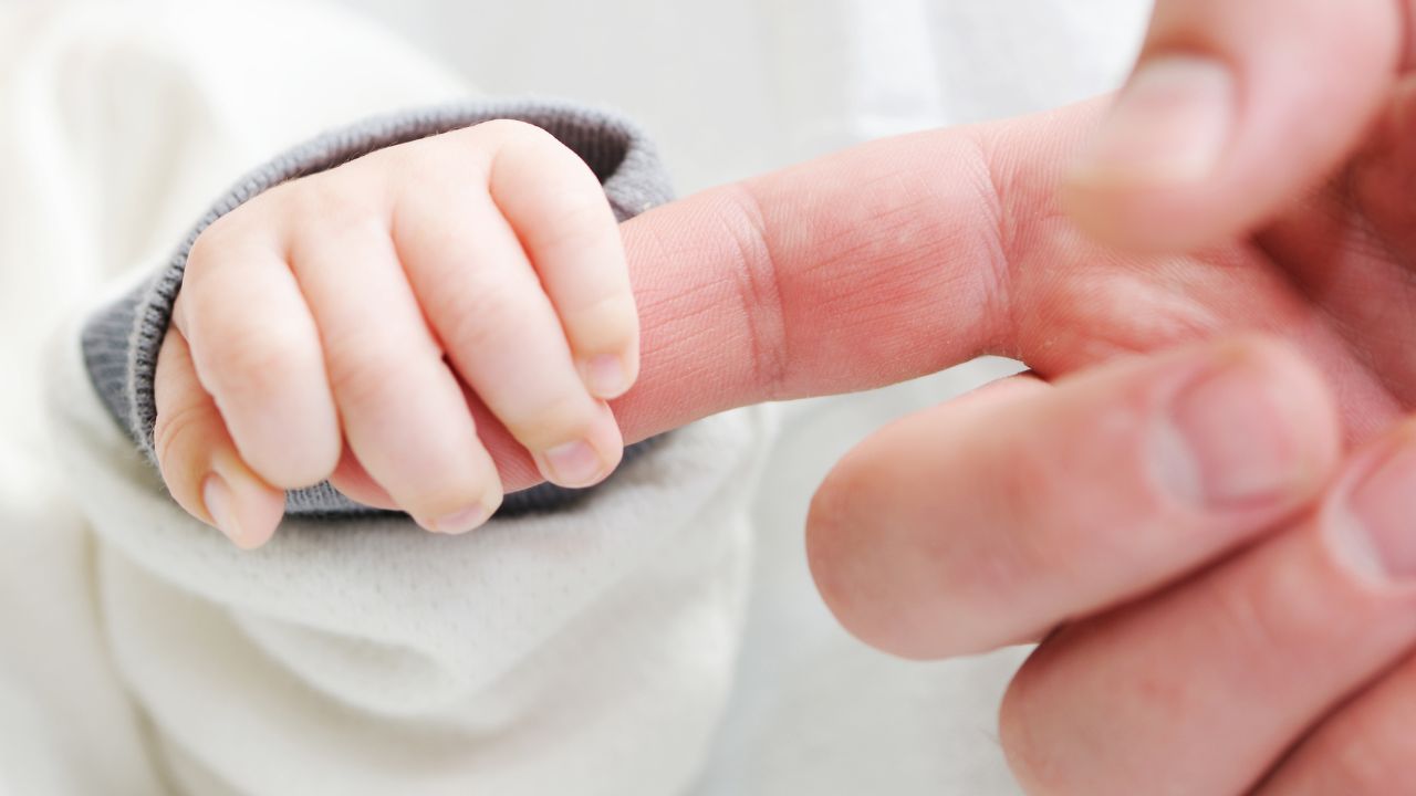 A baby holds onto her parent's index finger.