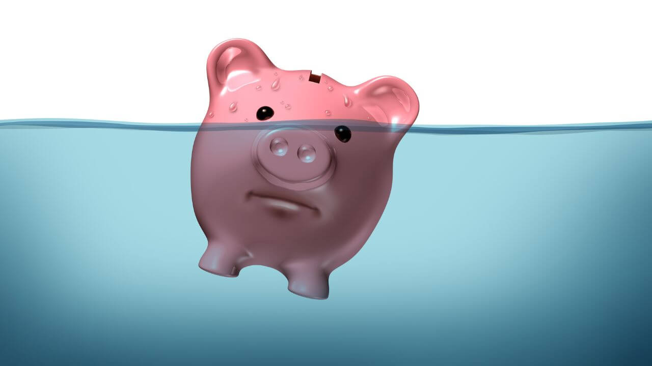 A pink piggy bank with an unhappy expression is mostly submerged underwater, with only one eye and ears visible above.