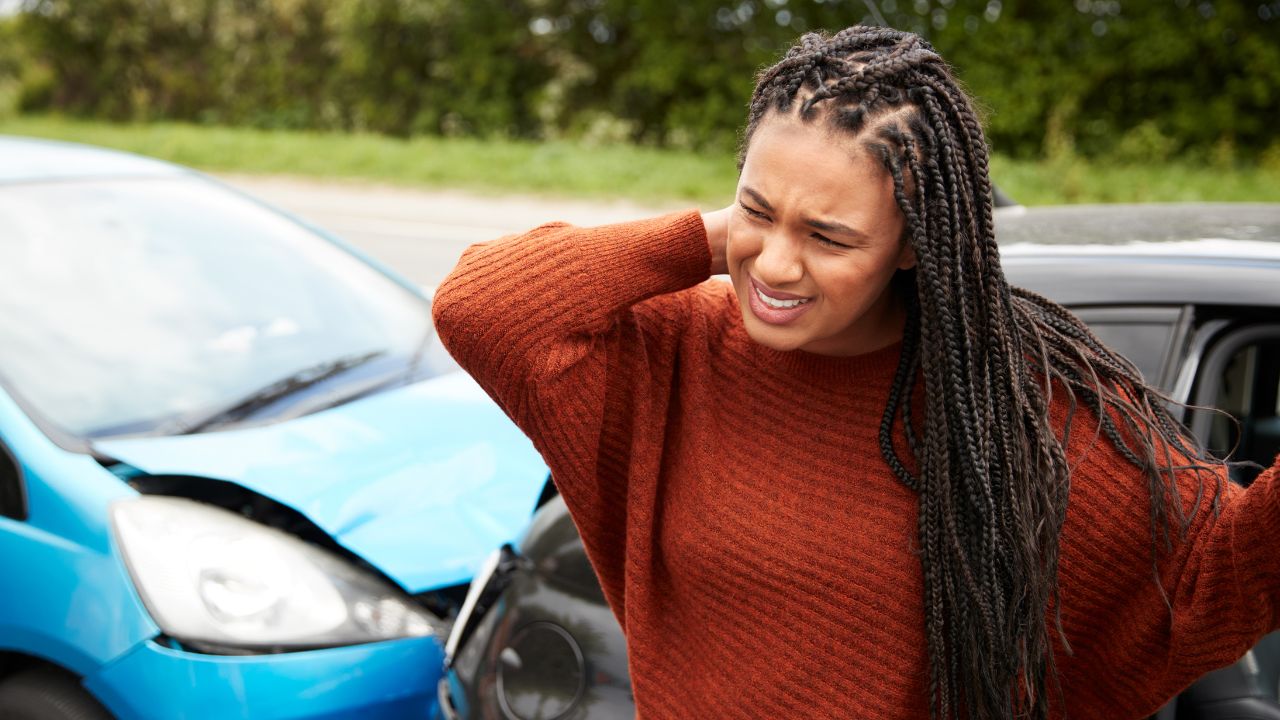 A woman holding her neck in pain at the site of a car accident.