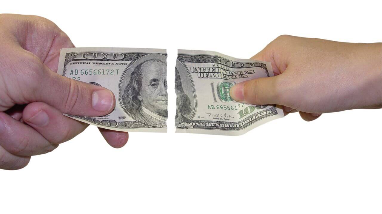 two hands each holding one half of a ripped $100 bill.