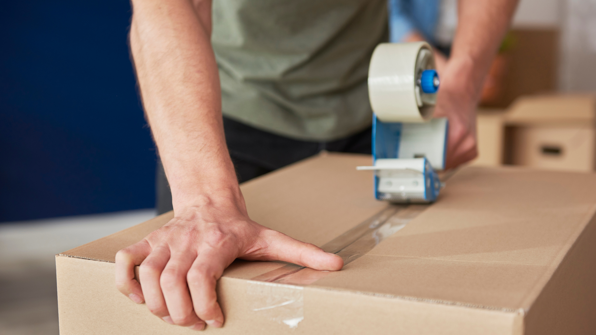 A man using packing take to seal a box closed.