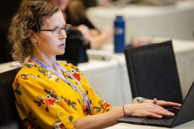 Woman in yellow typing at computer in conference space