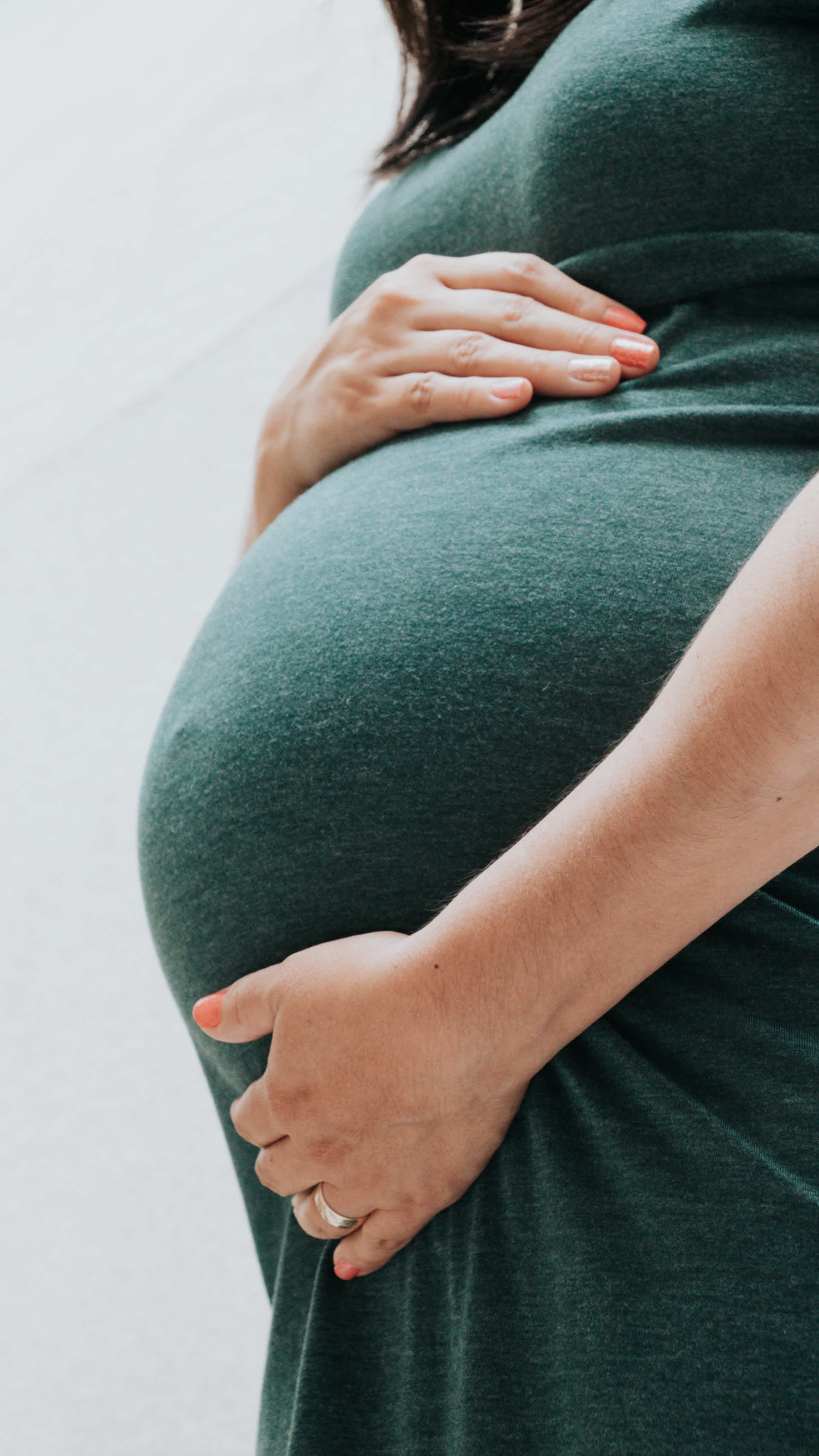 Pregnant woman in green dress holding tummy