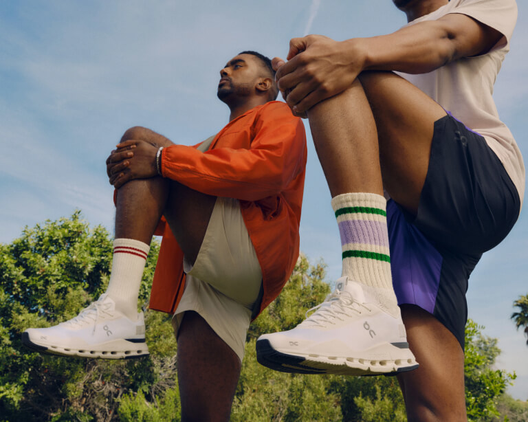 A pair of athletes stretch, wearing On running shoes.