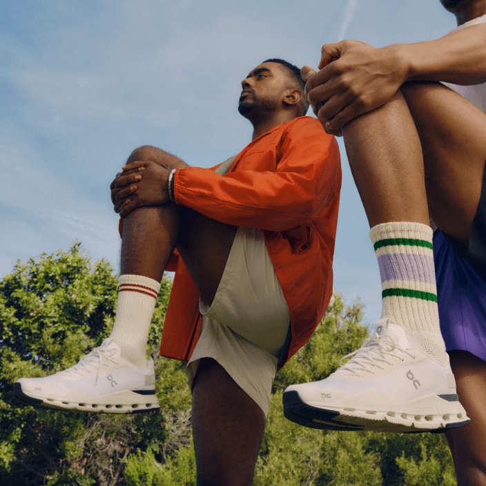 A pair of athletes stretch, wearing On running shoes.