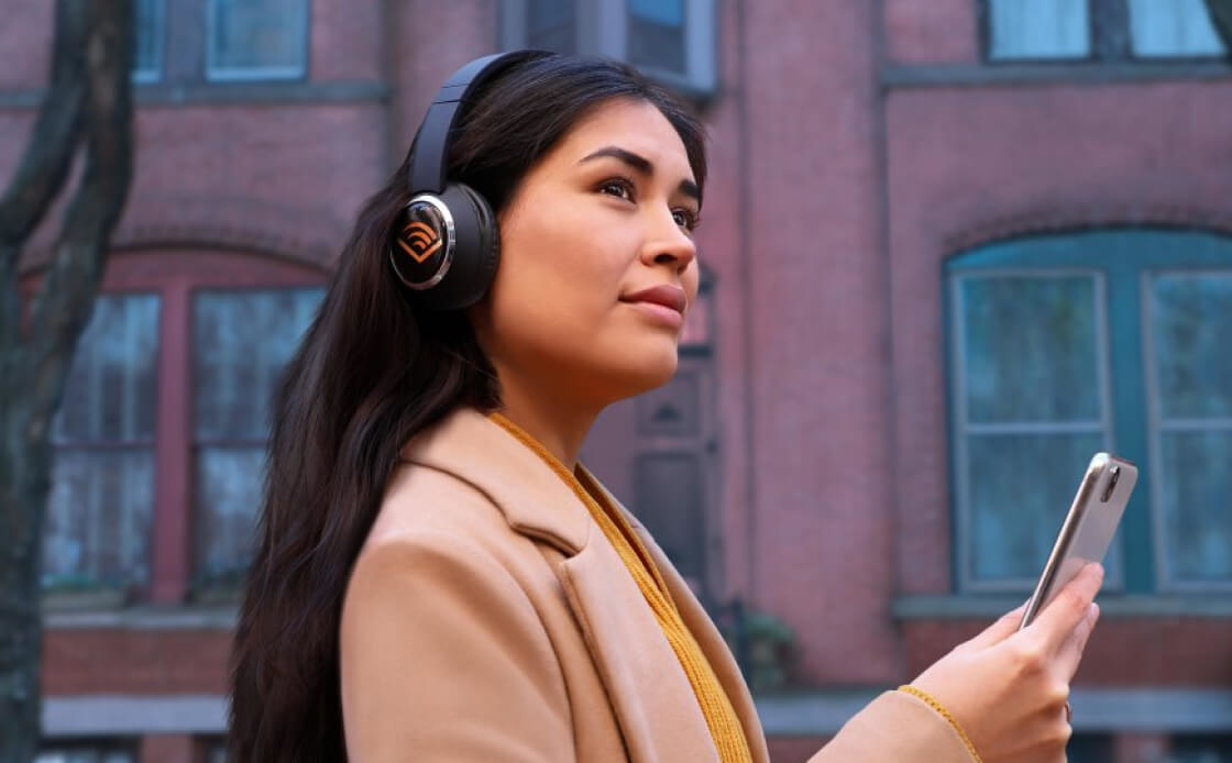 Female listening to Audible, wearing headphones and holding her phone