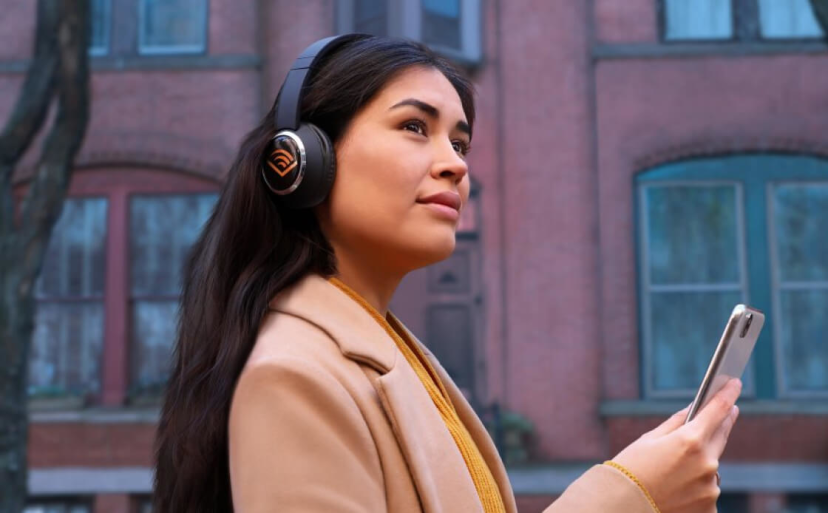 Female listening to Audible, wearing headphones and holding her phone