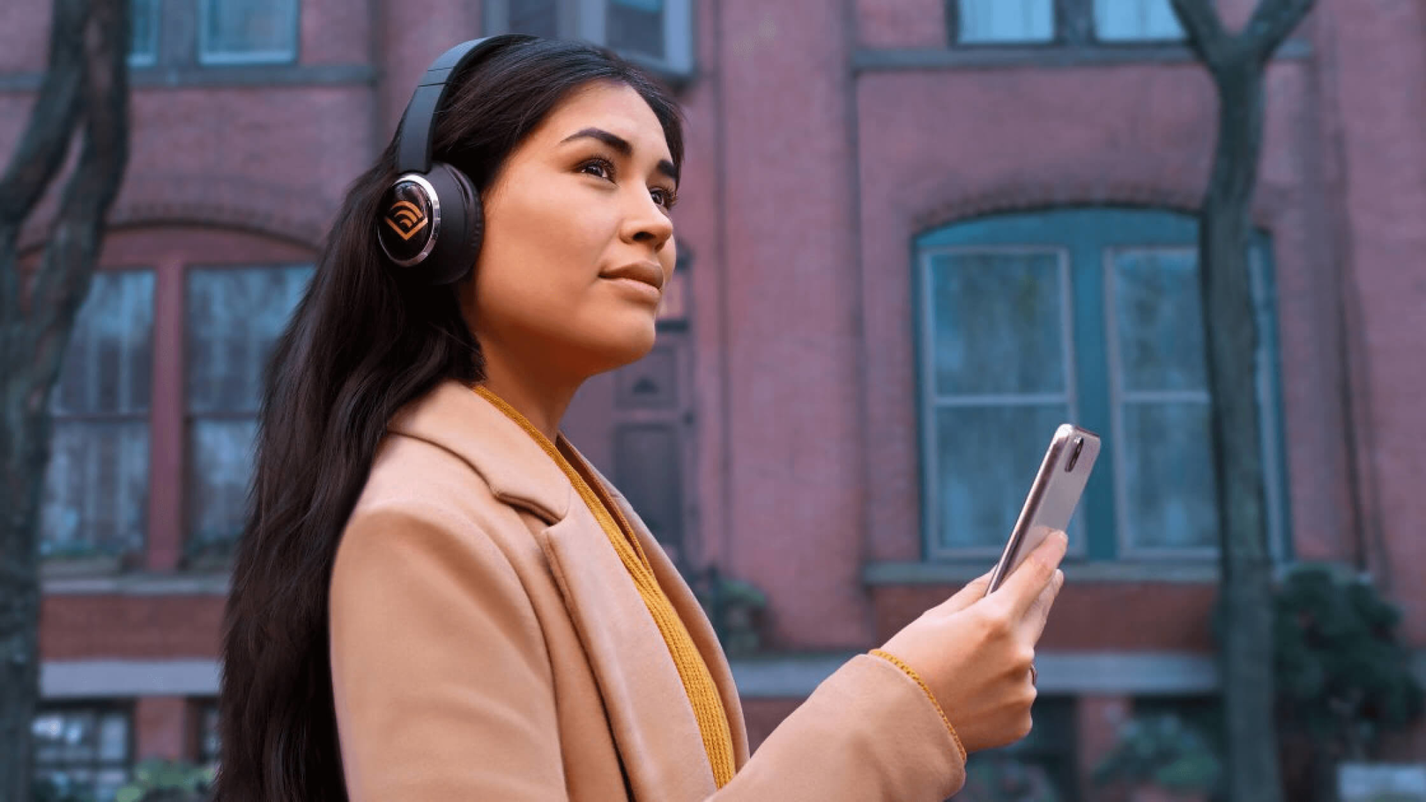 Female listening to Audible, wearing headphones and holding her phone