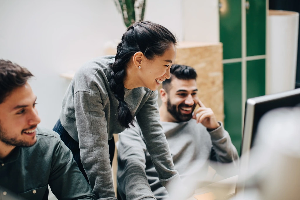 Two young professionals in casual grey sweaters share a genuine laugh while collaborating in a bright office space