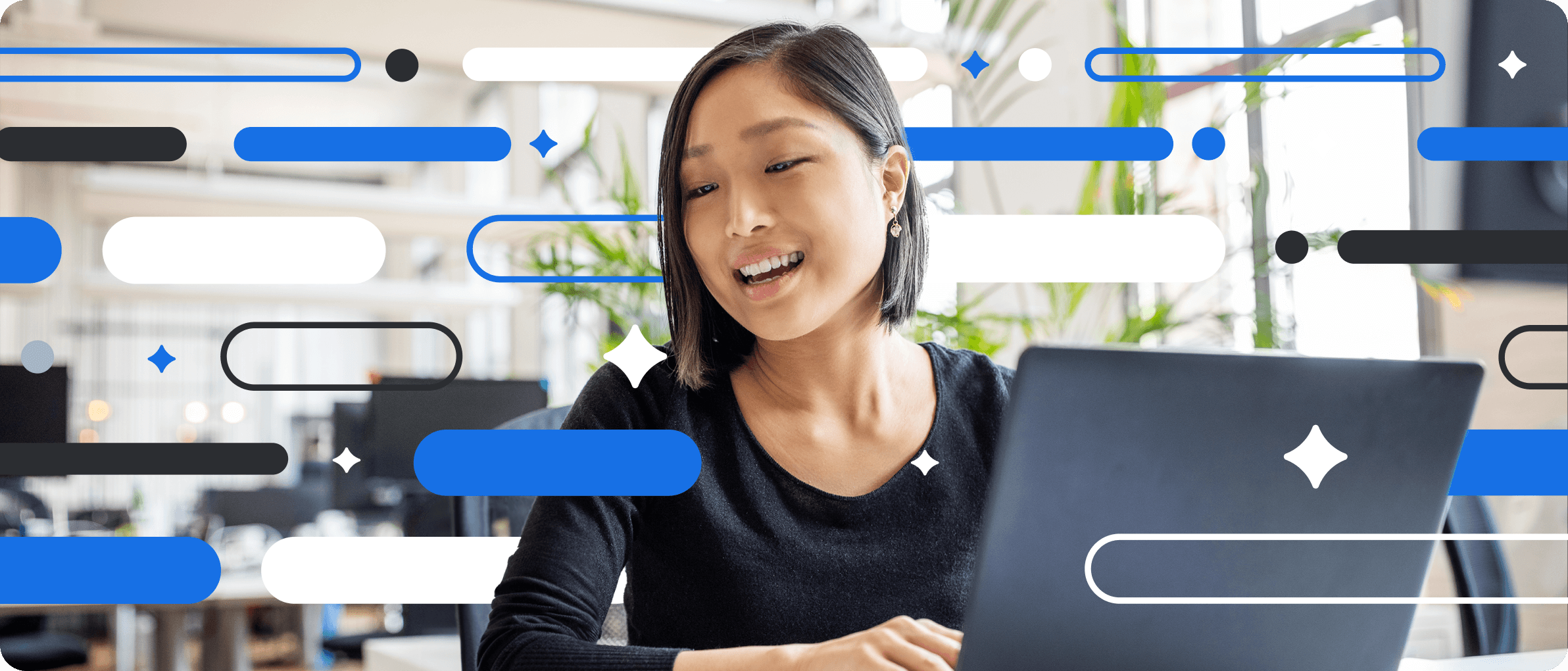 Professional in black sweater smiles while working on laptop in bright office with decorative blue and white graphic elements