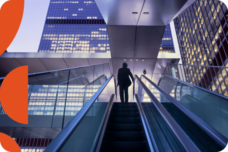 Business person ascending escalator in modern office building with illuminated glass skyscrapers visible through atrium ceiling