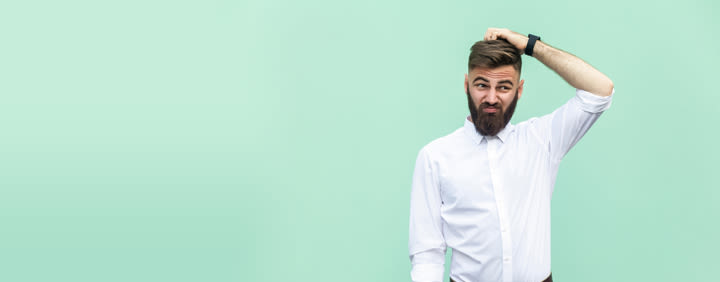 A man with a beard looking perplexed and scratching his head against a light green background.