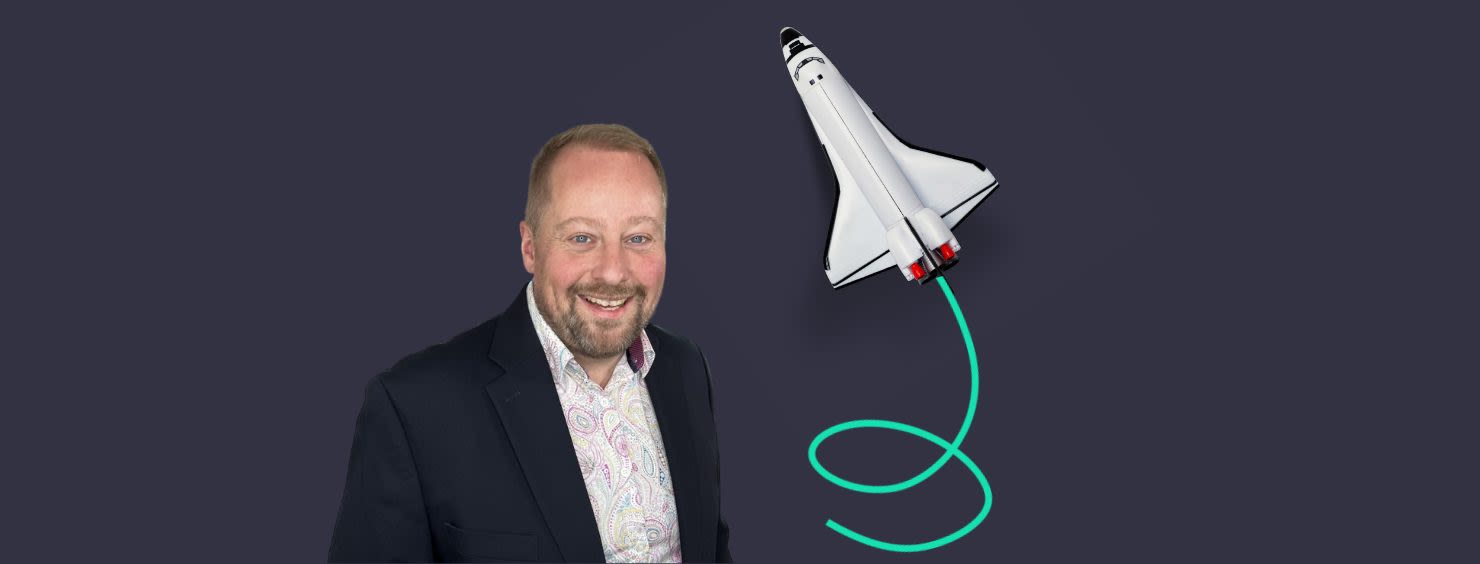 A man in a suit smiles next to a cartoon-like spaceship with a green trail on a dark blue background.