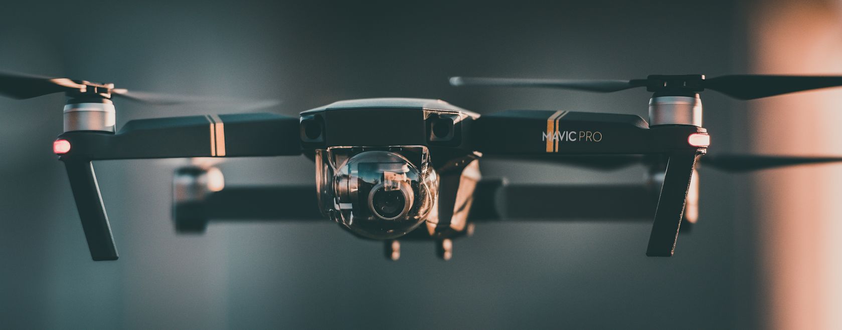 Close-up of a black DJI Mavic Pro drone with gold accents, featuring a clear protective camera dome and glowing red lights at the end of its arms.