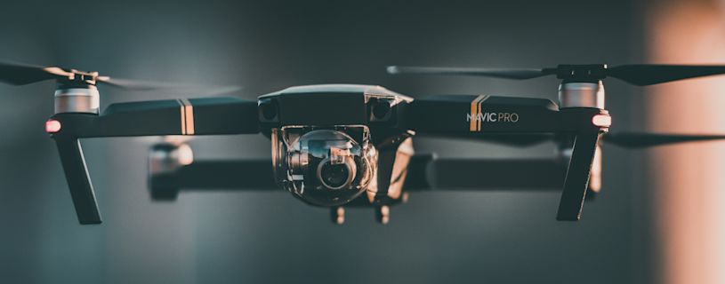 Close-up of a black DJI Mavic Pro drone with gold accents, featuring a clear protective camera dome and glowing red lights at the end of its arms.