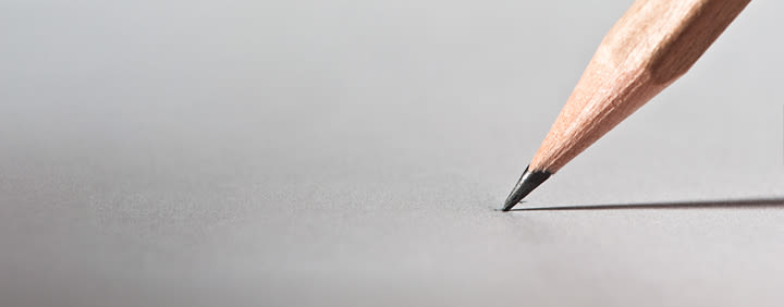 Close-up of a pencil point touching a white sheet of paper, casting a shadow.