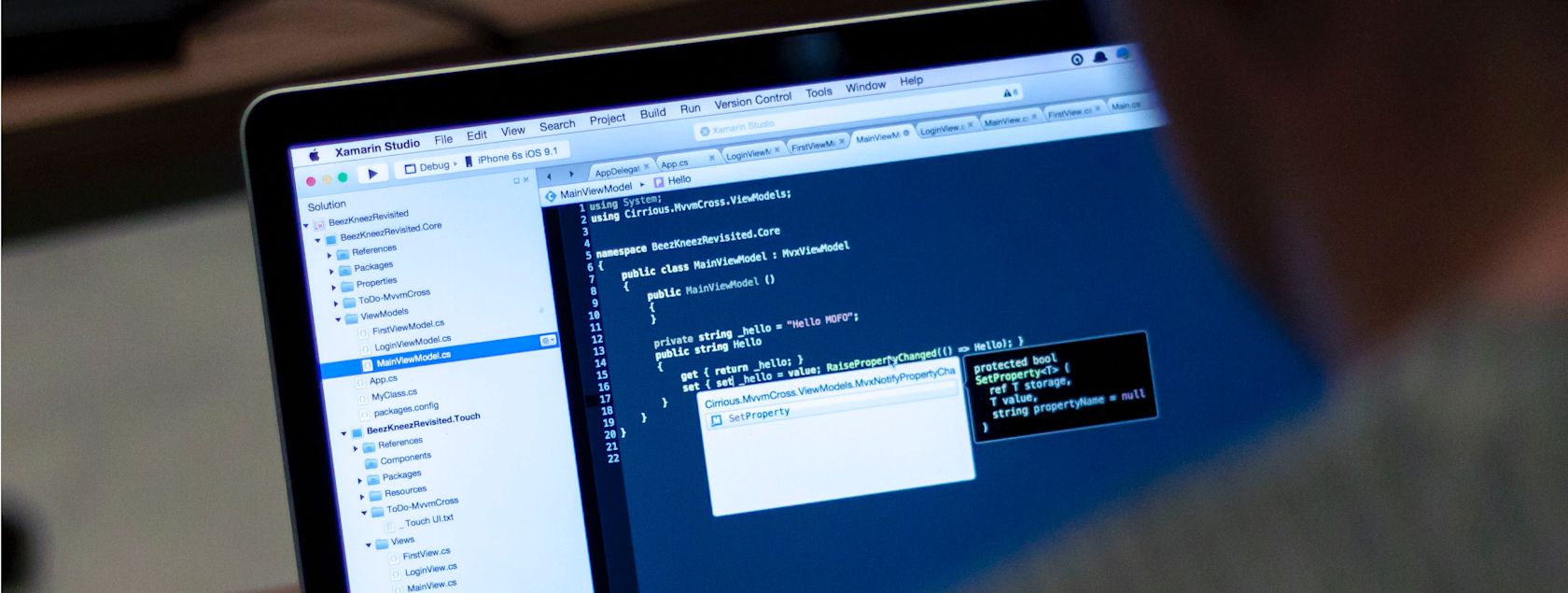 A laptop displaying Xamarin Studio IDE, showing C# code for a mobile application.