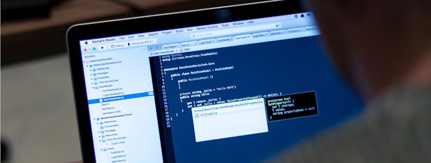 A laptop displaying Xamarin Studio IDE, showing C# code for a mobile application.